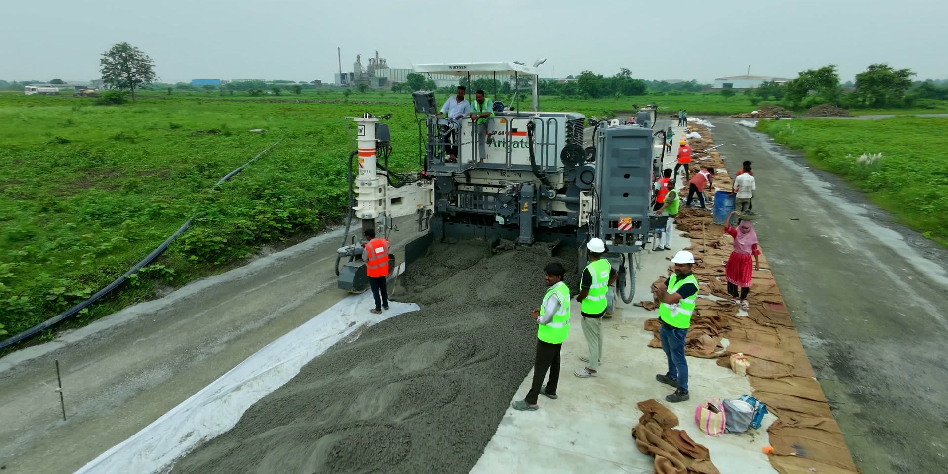 Aerial view of a slipform paver laying a cement concrete carriageway, with the site crew working alongside it.